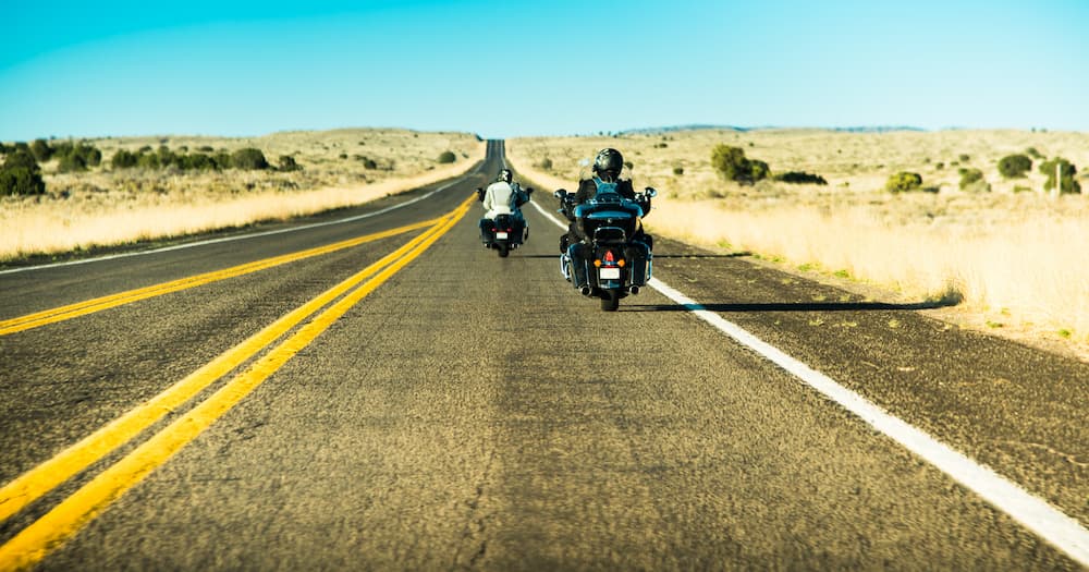 two motorcycles riding on an open highway with fields on either side